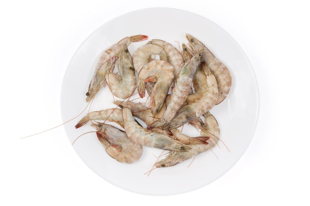 Heap of frozen ocean king prawns on big white dish on a white background, top view